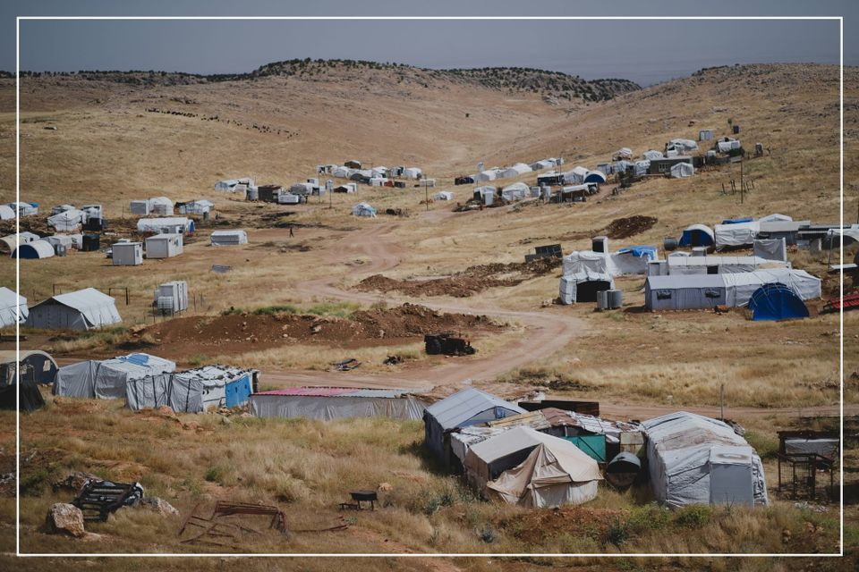 “A sprawling refugee camp in a dry, hilly landscape. Rows of tents and shelters stretch into the distance, capturing the scale and humanity of global displacement.”