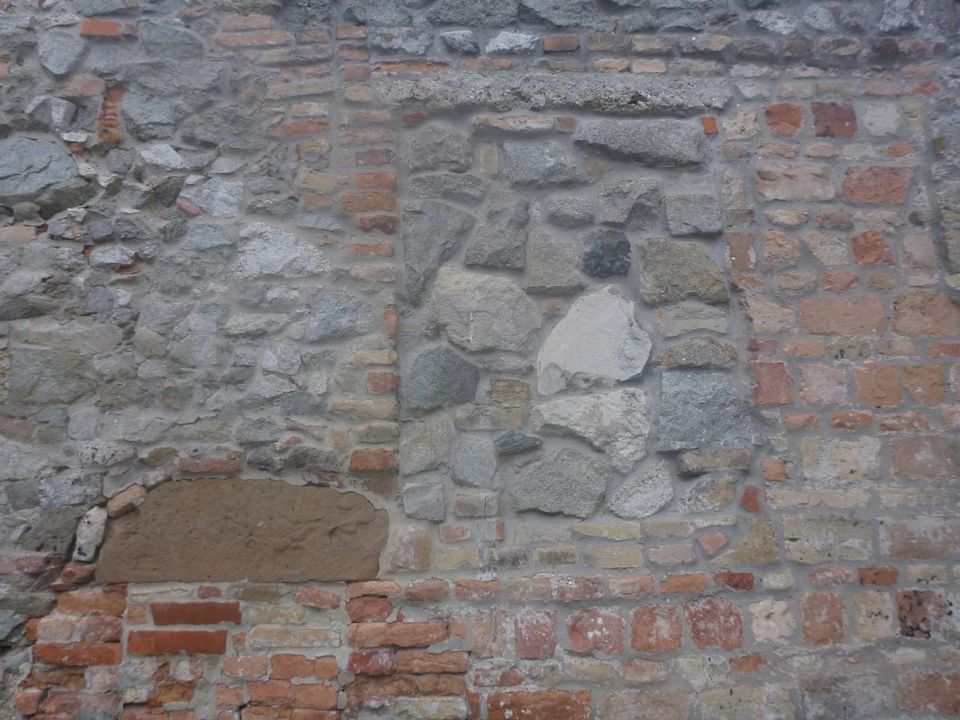 Close-up of an old stone wall patched together from many eras, its uneven bricks and mismatched stones forming a single weathered structure.