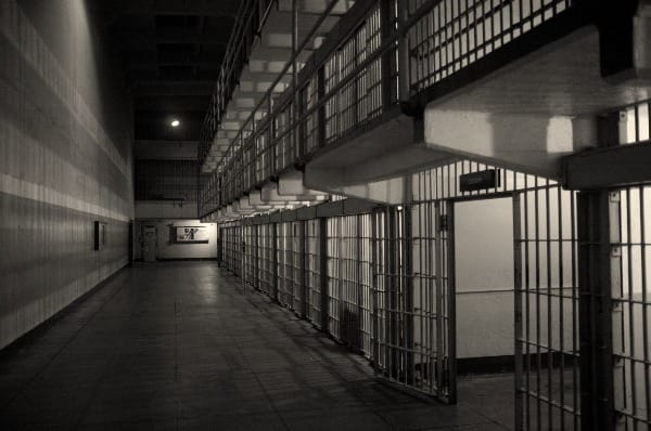 A row of prison cells, one door open.