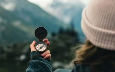 girl outdoors near a mountain looks at her compass to determine direction