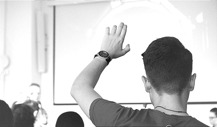 man wearing black t-shirt raises his hand in a meeting room