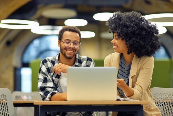 two smiling colleagues near a single computer, showcasing teamwork.