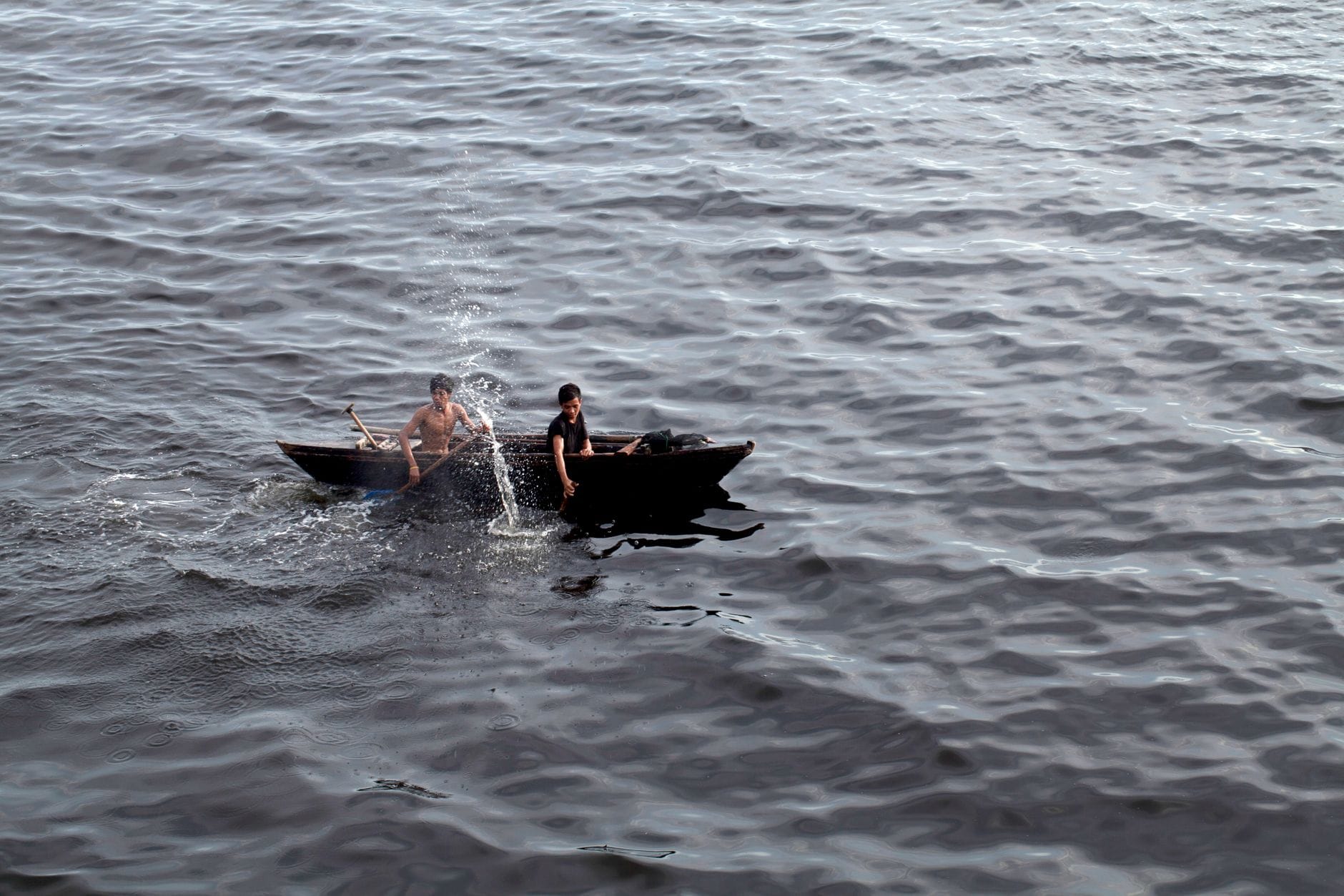 Two men in a small boat fishing on rippling water surface, natural scene.