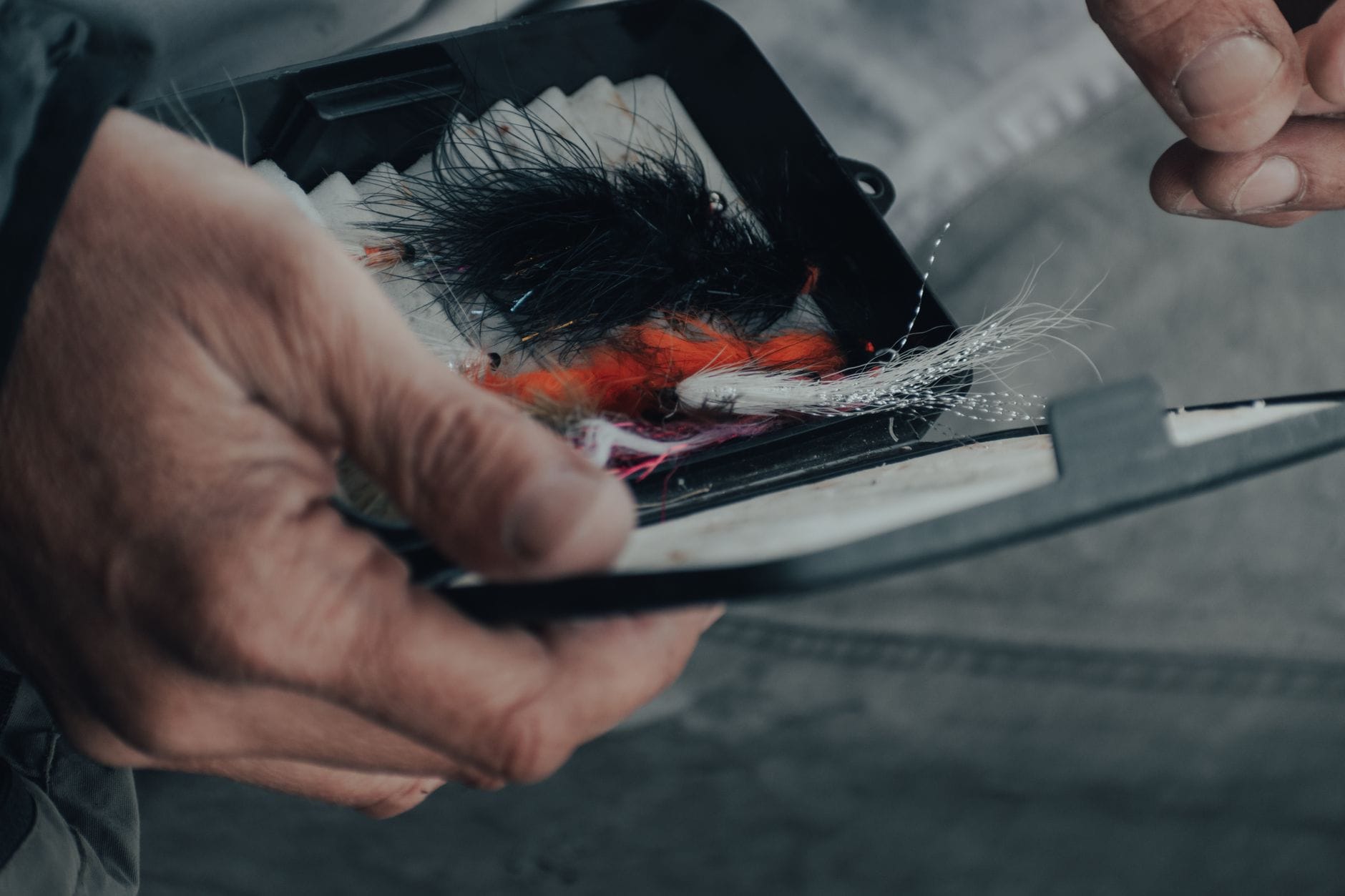 Detailed view of hands selecting colorful fishing lures from a tackle box outdoors.