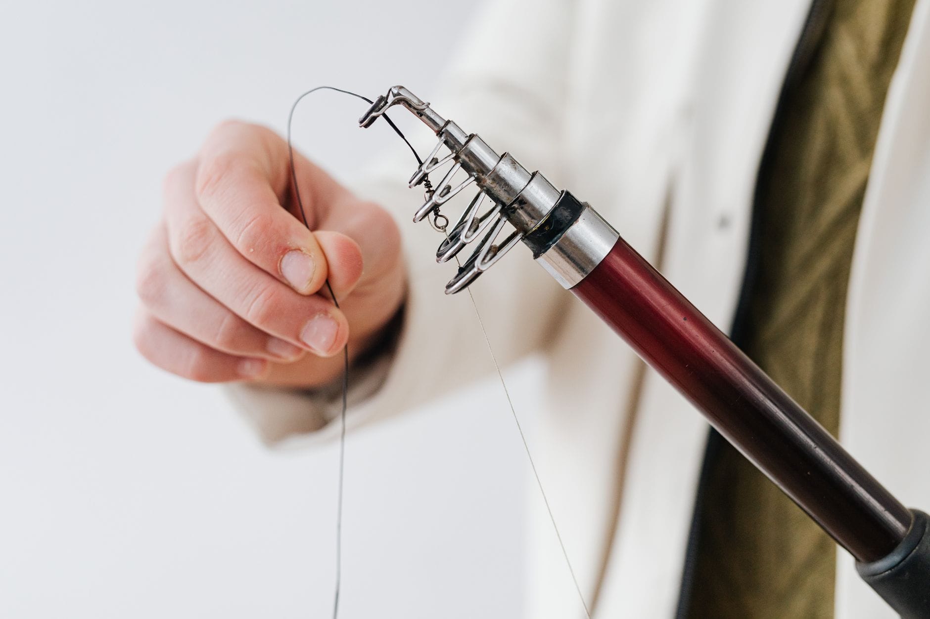 Detailed shot of a hand preparing a fishing rod with line indoors.