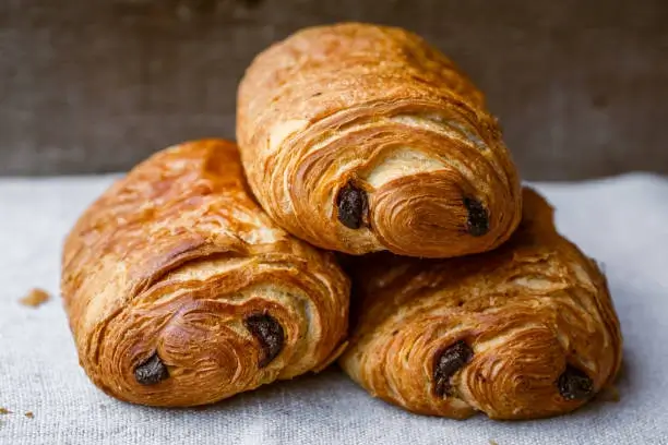 Three pain au chocolats piled on a gray tablecloth
