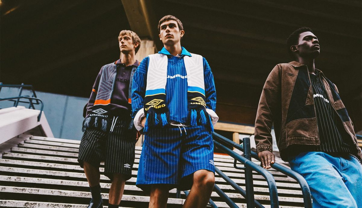 Model in Umbro AW26 Away Days pinstripe drill top and trench coat at a train platform