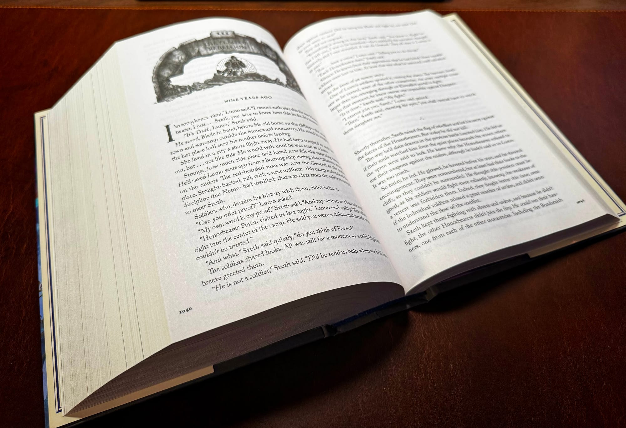 An open hardcover book resting on a brown surface, showing two pages of text. The left page includes a chapter heading labeled “Nine Years Ago” with an illustrated header above it, while the right page continues the story in dense paragraphs.