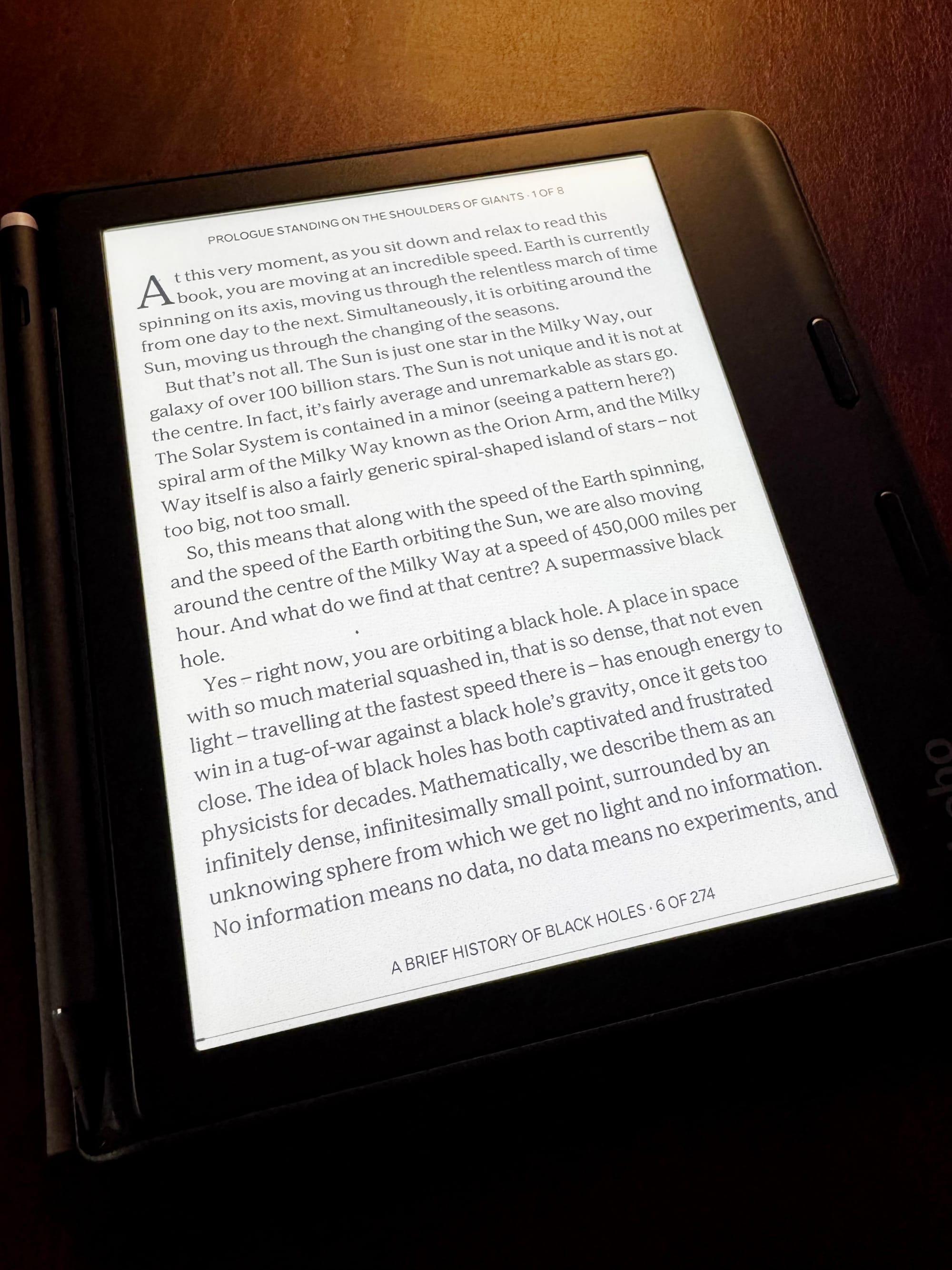 An e-reader on a brown surface displaying text from the book A Brief History of Black Holes.