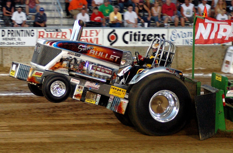 Image of a high horsepower "tractor" with it's front end lifted off the ground in a tractor pull competition.