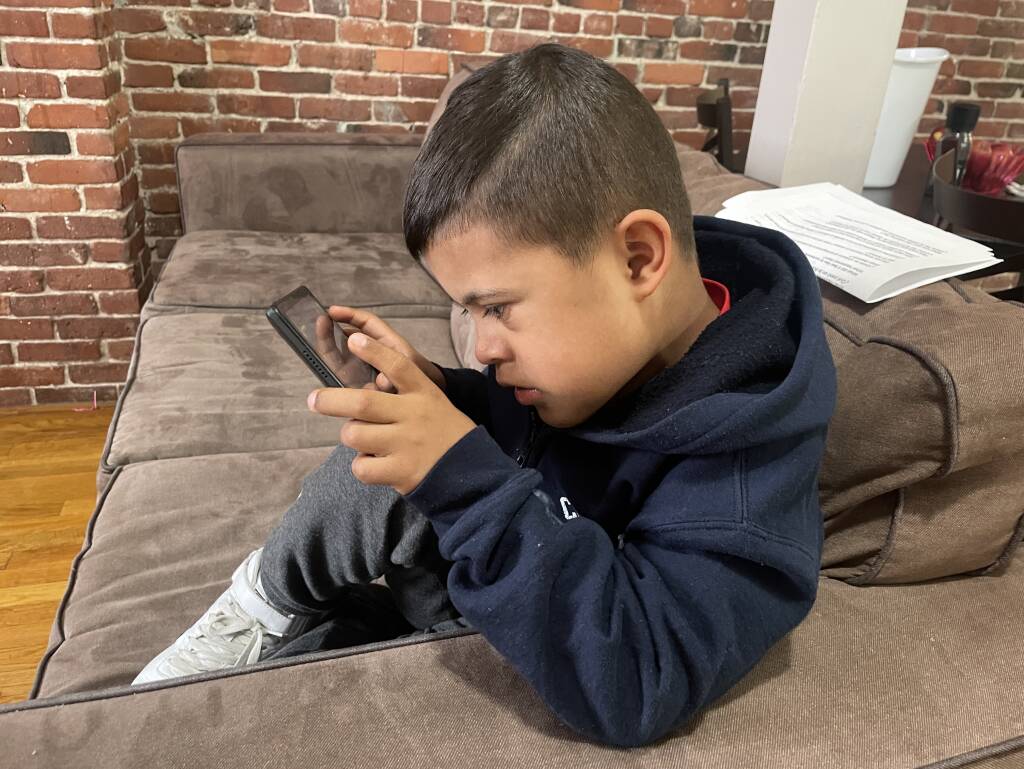 Freydar Torres, de 7 años, juega fútbol en un iPad, mientras su padre, Freddy, lava los platos.
Foto de Sarah Betancourt, GBH Noticias
