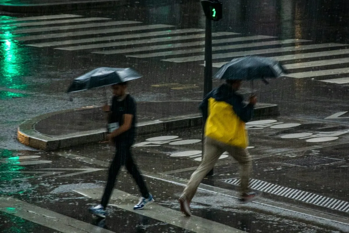 Personas caminan bajo la lluvia con paraguas en una calle de la ciudad