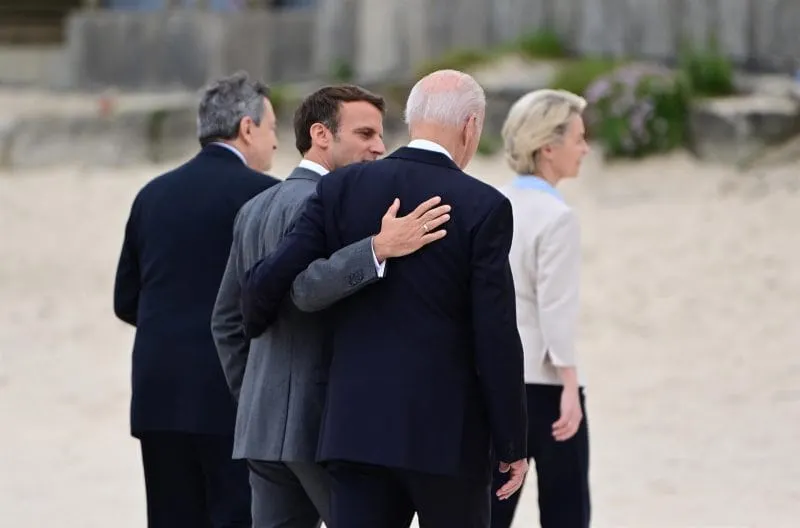 CUMBRE. El presidente de Estados Unidos, Joe Biden (d); y el presidente de Francia, Emmanuel Macron, caminan abrazados por el