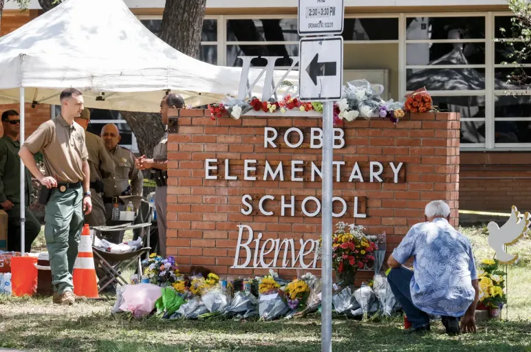 Un hombre se arrodilla junto a un monumento de flores en el lugar de un tiroteo masivo en la Escuela Primaria Robb en Uvalde,