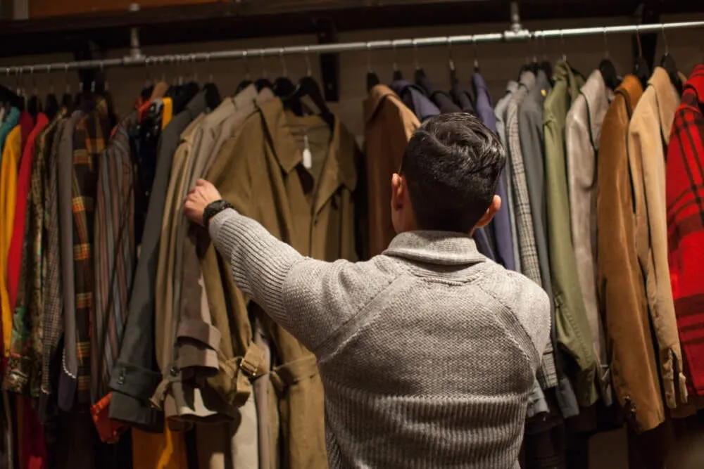Joven hombre buscando entre las prendas en un negocio de ropa vintage. Foto: Getty Images.