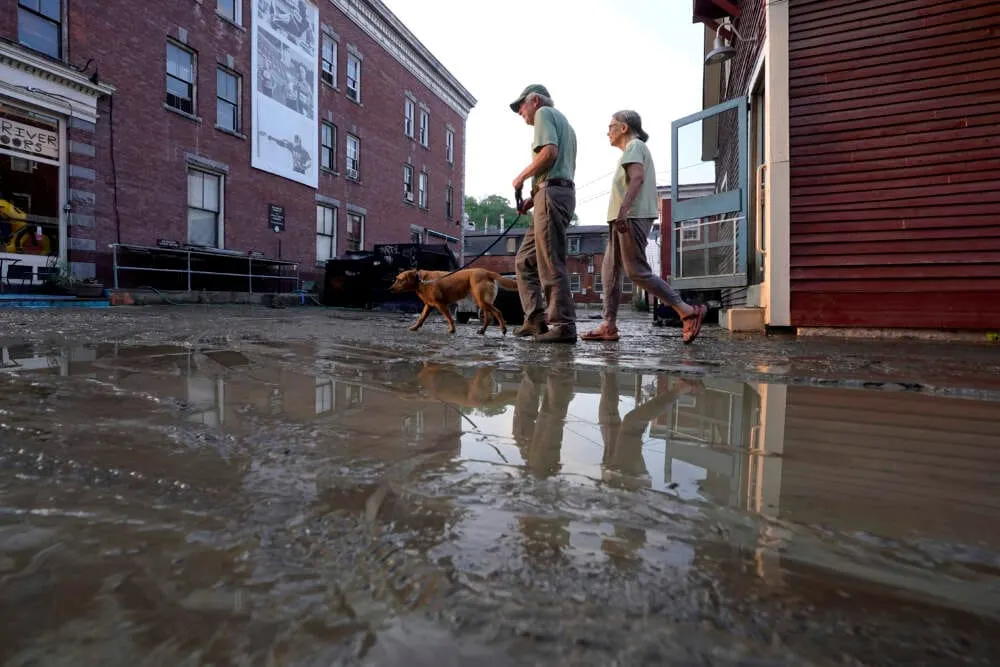 La gente pasea a un perro en una calle embarrada el martes 11 de julio de 2023 en Montpelier, Vt. Una tormenta que arrojó has