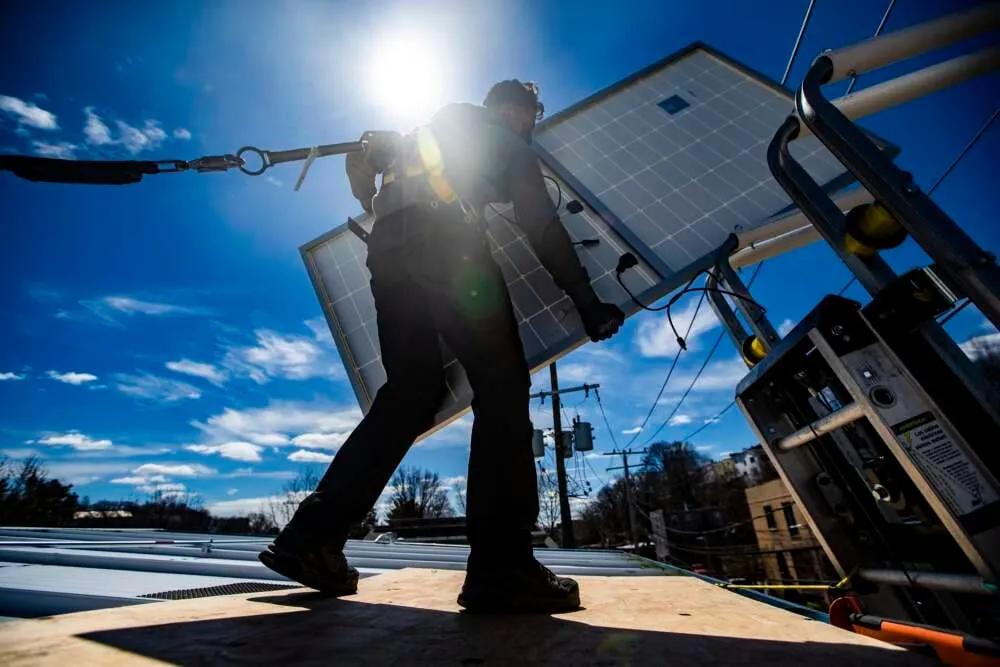 Un técnico retira un panel solar de una plataforma durante la instalación de paneles solares en el techo de Boston Building R