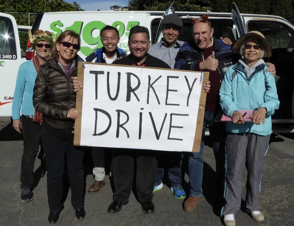 A group pf volunteers pose with a sign reading "Turkey Drive."