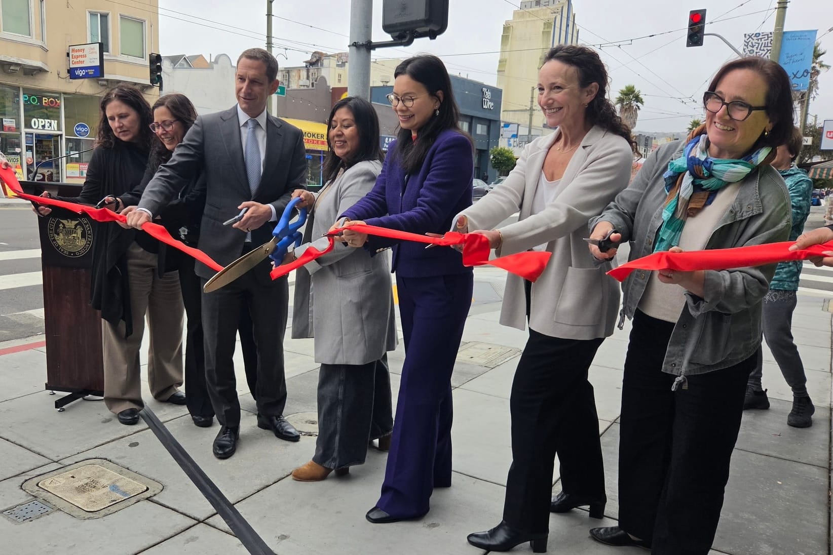 Seven people cutting a red ribbon.