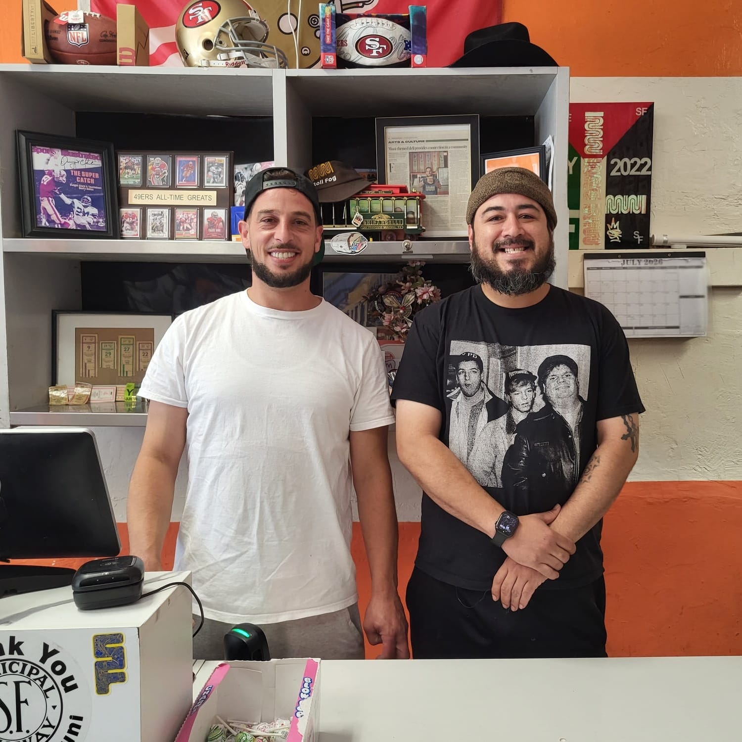 Two men pose for a picture behind a counter.