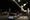 Man walks on sidewalk under string lights.