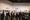 A crowd of casually and black-tie dressed people looking at art pieces on a large white wall.