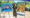 A woman standing outside in a black dress with yellow tulips and in between her brightly colored abstract paintings.
