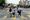 Two women walk with a kid on a scooter while holding flower shaped balloons in the middle of a busy closed street.