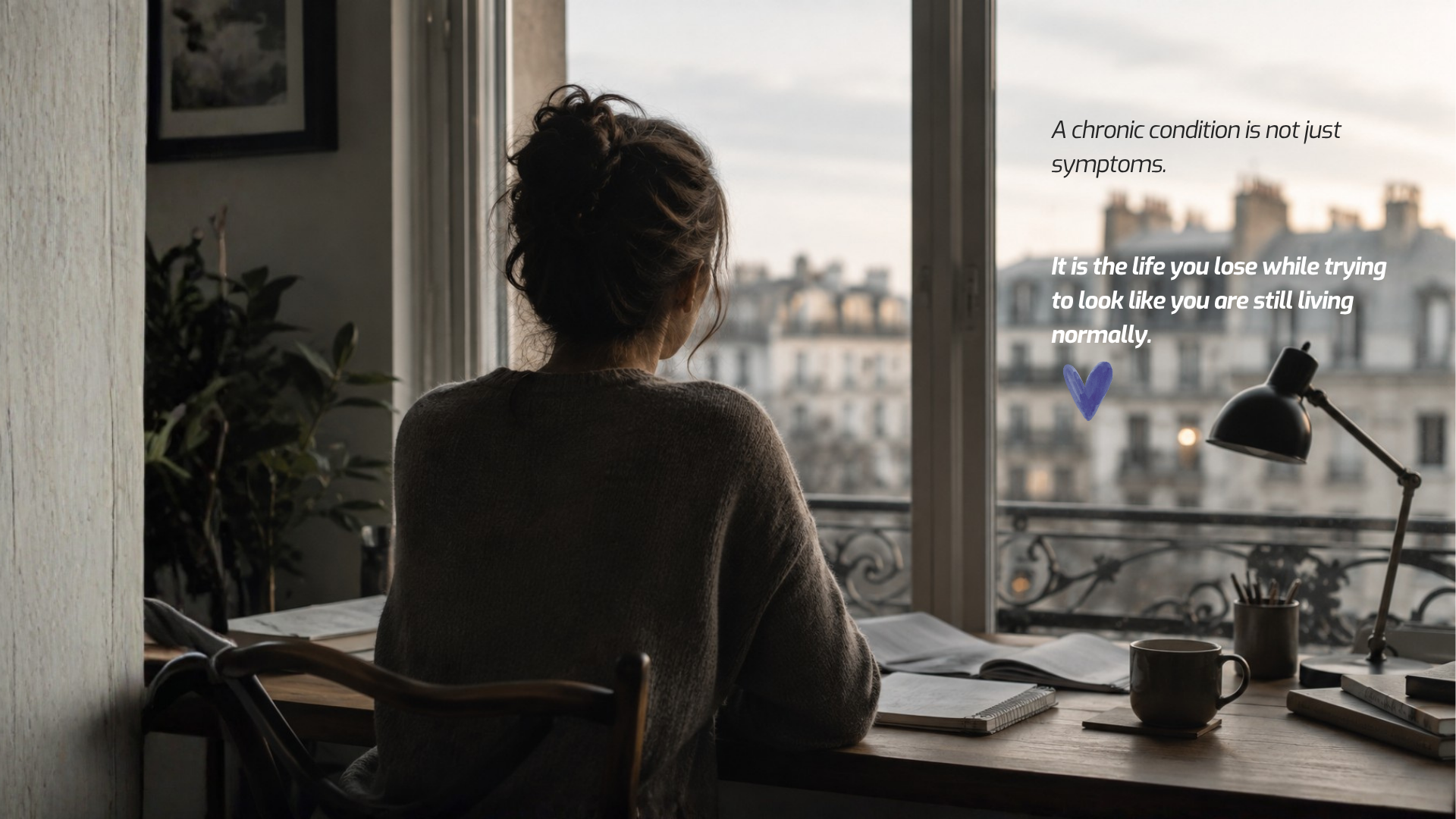 Woman seen from behind sitting near a window, looking outside while working quietly at a table.