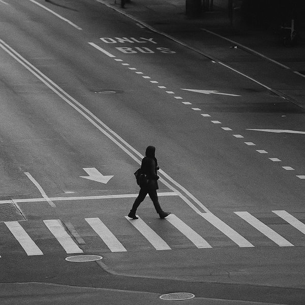 A black and white photo of a person crossing a street