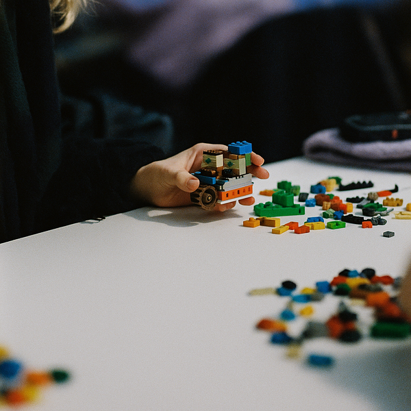A person building with colorful lego bricks on a white table.