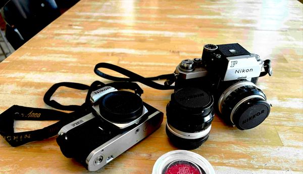 Film cameras and a lens on a wooden table, the analog tools of a writer exploring AI-assisted publishing.