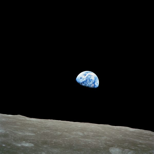 Earth photographed from lunar orbit: a blue and white sphere, roughly half in shadow, above the gray cratered curve of the Moon's horizon, with black space behind.