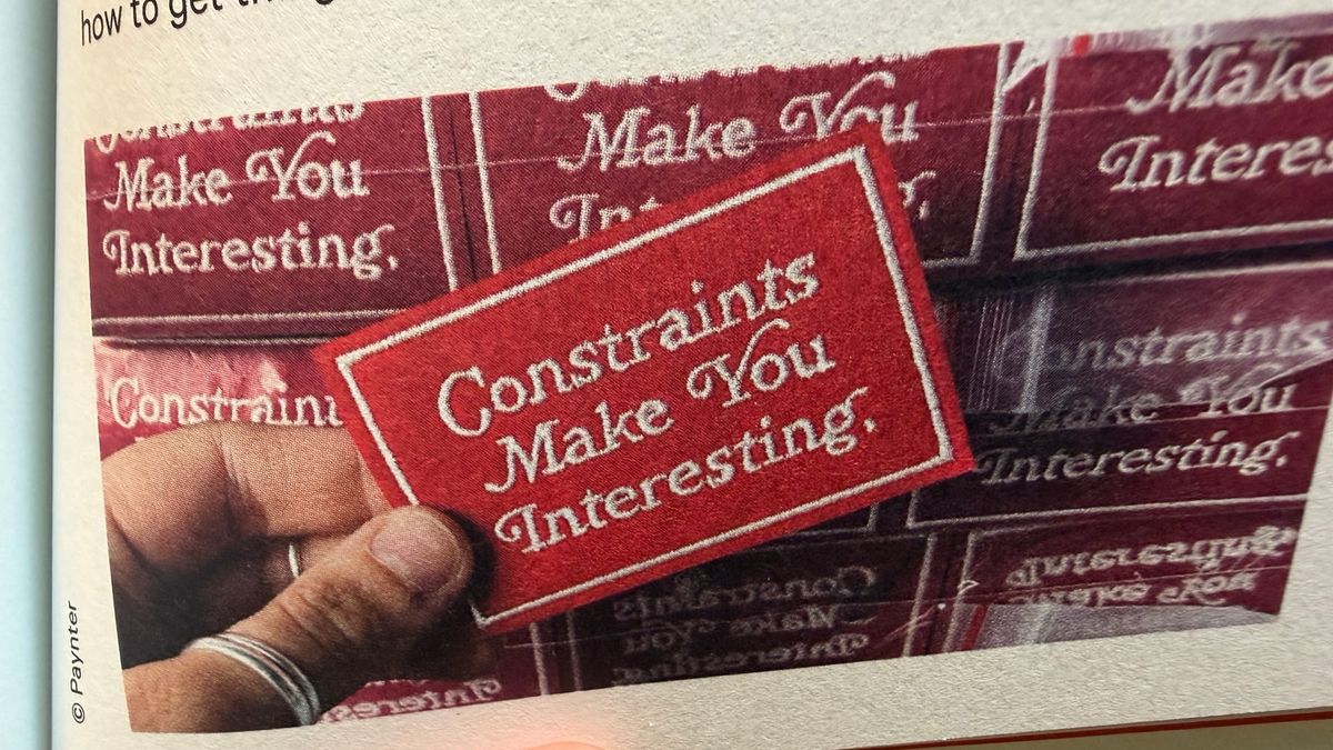 A hand holding a label saying 'constraints make you interesting'