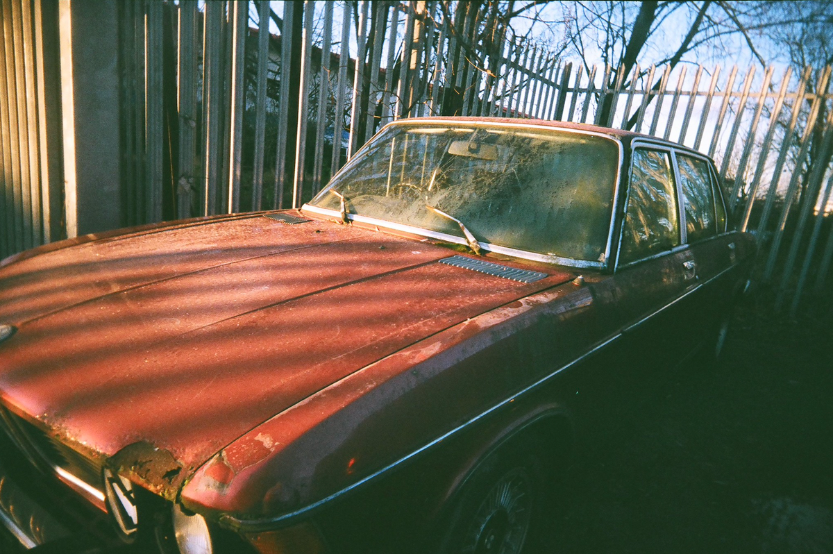 A rusty, and red, BMW that's been abandoned