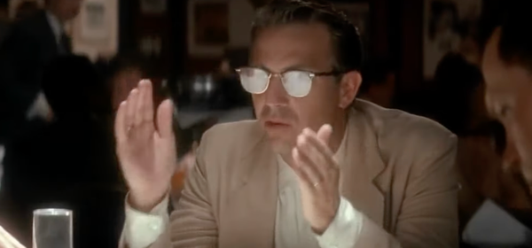A still of Kevin Costner from JFK, in sunglasses, holding his hands up, explaining something