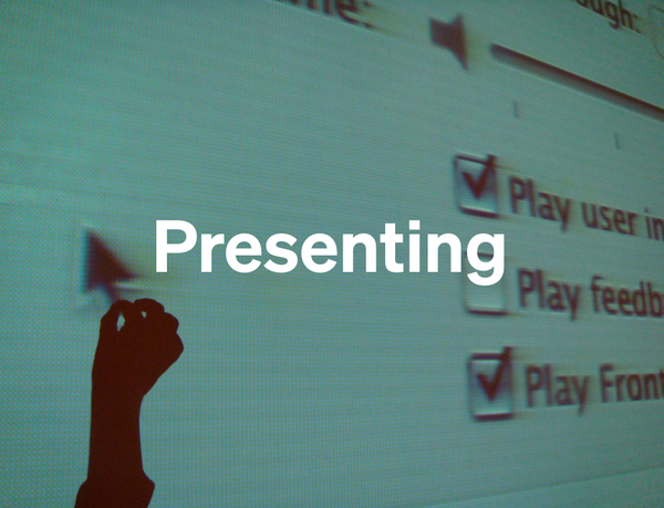 A projection of a computer screen with a hand appearing to hold the cursor and the word 'Presenting' superimposed on it