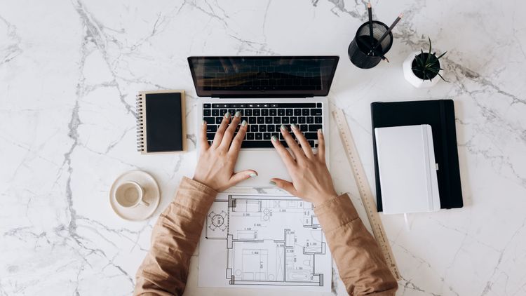 mesa de escritório de engenharia com objetos como agendas, computador e plantas por cima