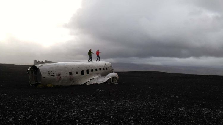 Two men standing on top of an old plane in Iceland with a surfing stance.