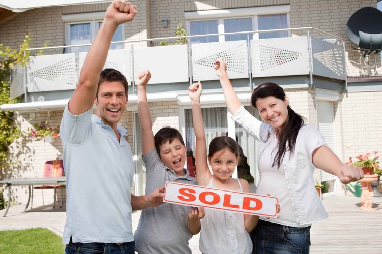 A family is standing outside on a sunny day holding a "sold" sign.