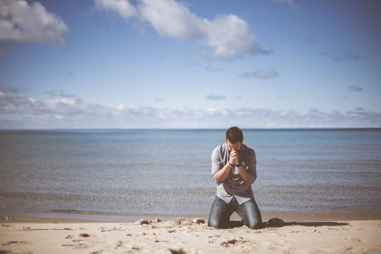 A man is kneeling in the sand by the ocean.