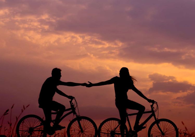 A couple riding bicycles and holding hands