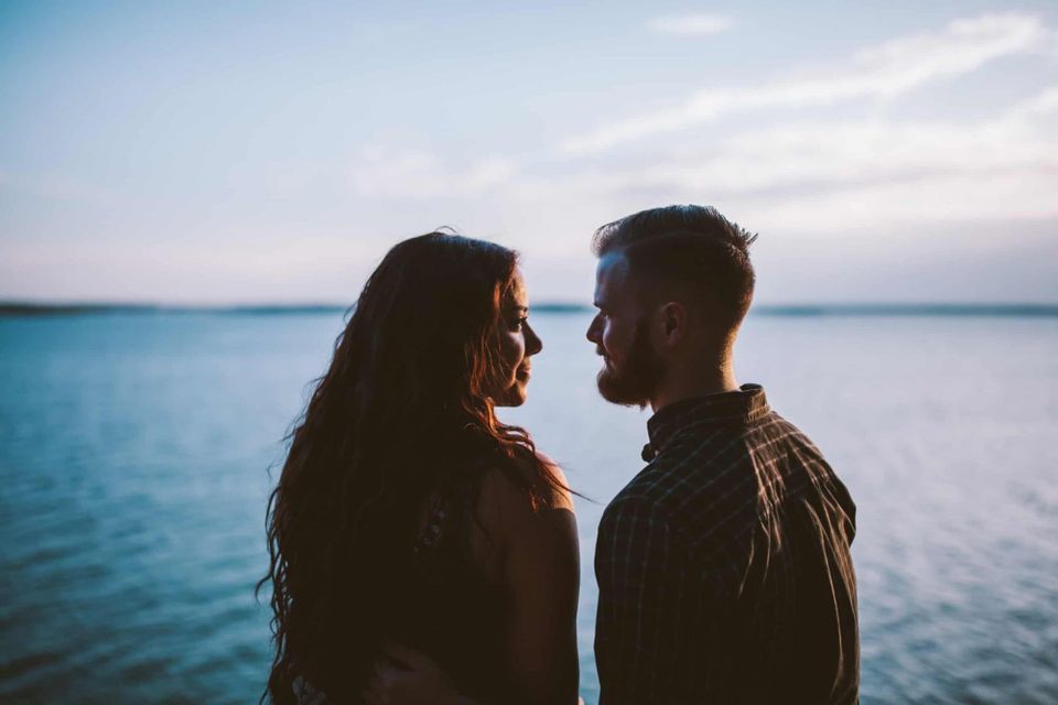 A romantic couple facing each other by a lake.