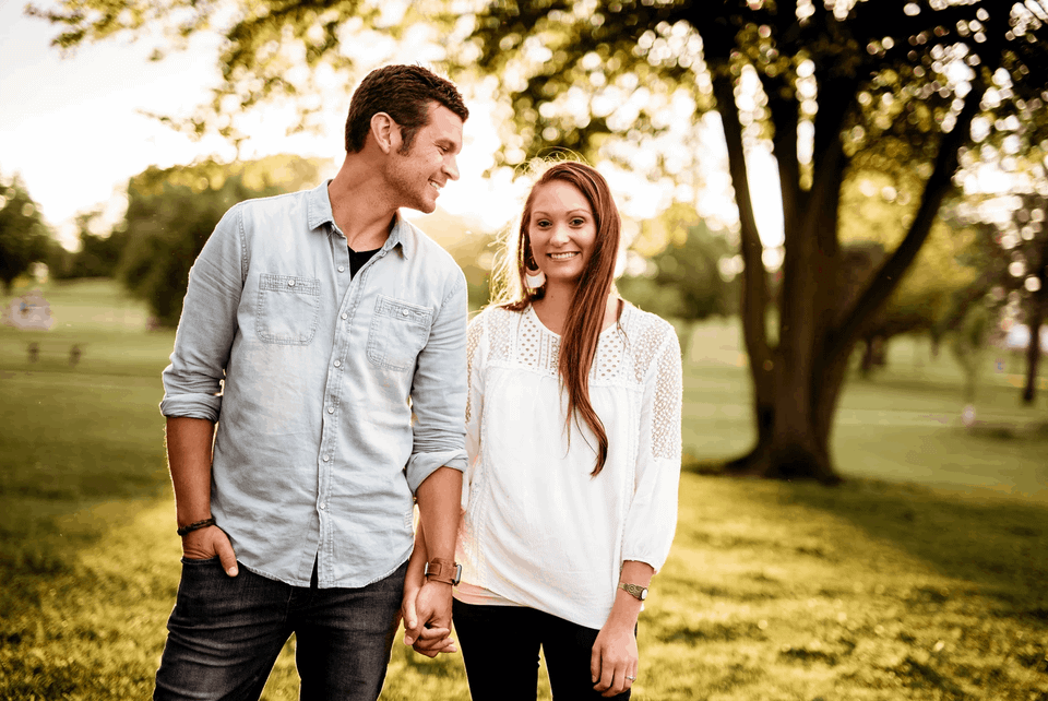 A married couple is holding hands and walking in the park as the sun is setting.