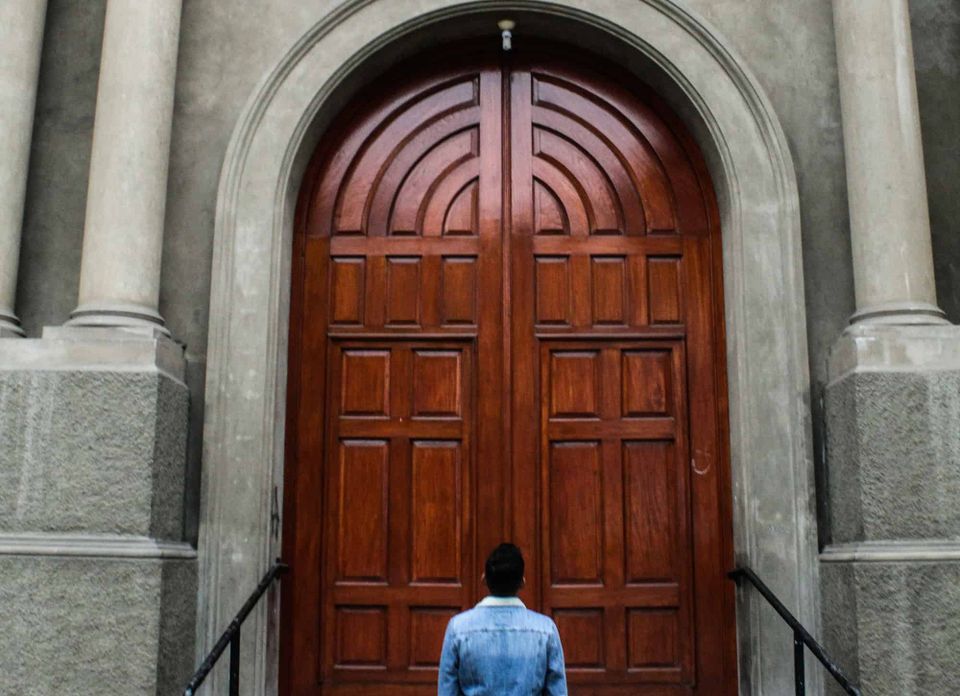 A man looking a big brown wooden door.