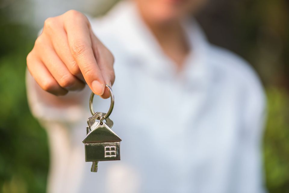 A man is holding a keychain with a house and key on it. 