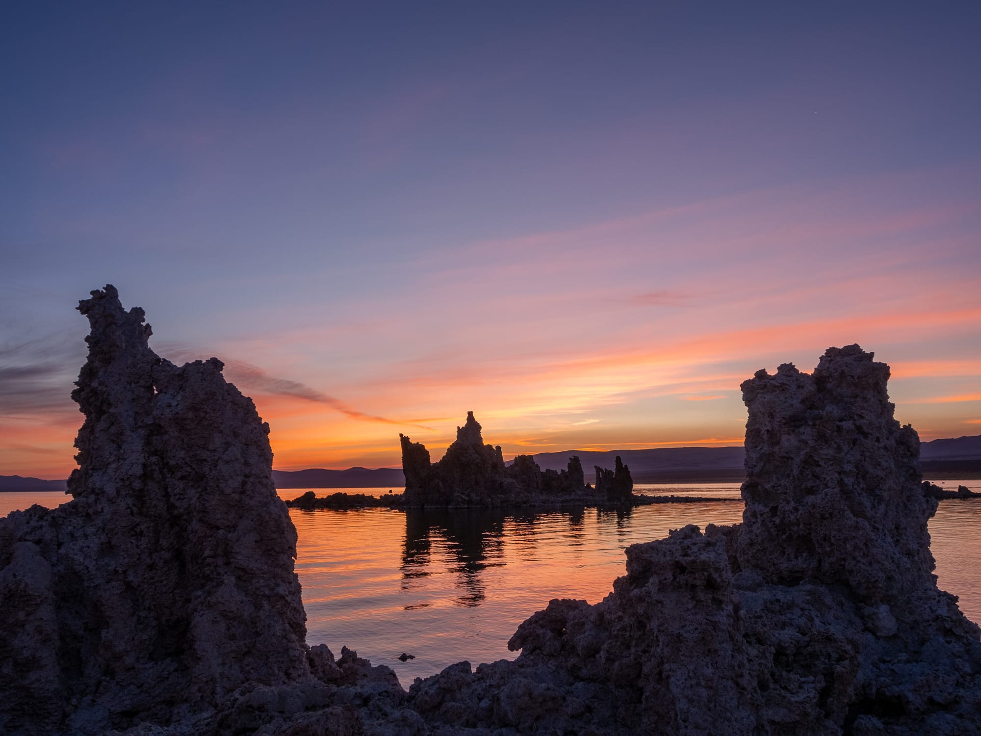 Two rock formations frame a castle like rock formation surrounded by water that is reflecting purple and orange from the sunrise above.