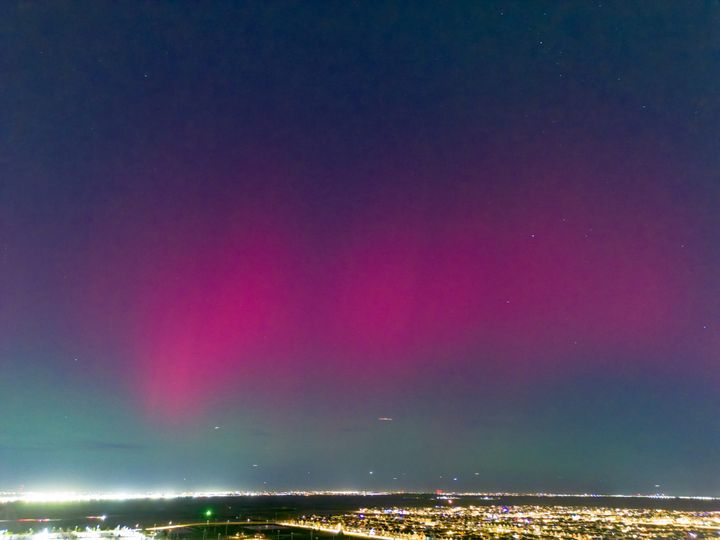 Red columns and a faint green glow in the sky are seen above city lights in an aerial photo.