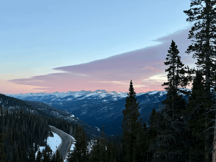Snowcapped mountains are visible in the distance under a light blue sky with purple and pink clouds. 