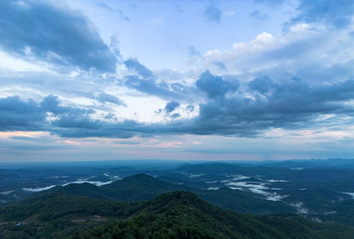 Rolling green mountains under cloudy sunset skies. A low fog sits in distant valleys. 